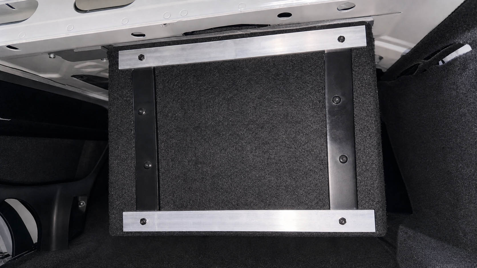 AI-assisted visualization of a carpeted prototype enclosure suspended beneath a vehicle rear deck with aluminum support bars.
