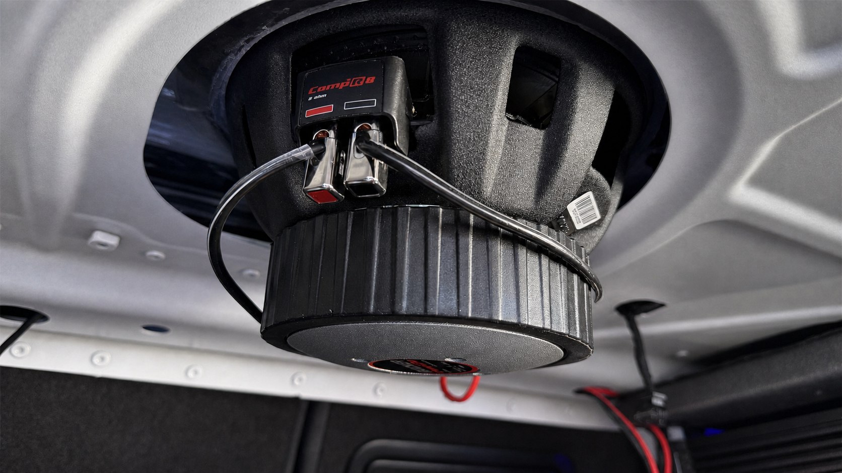 Close view of a subwoofer prototype mounted beneath a vehicle rear deck.